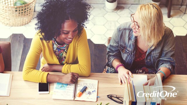 Two female college students smile at each other as they study together, perhaps learning some tips for building credit.